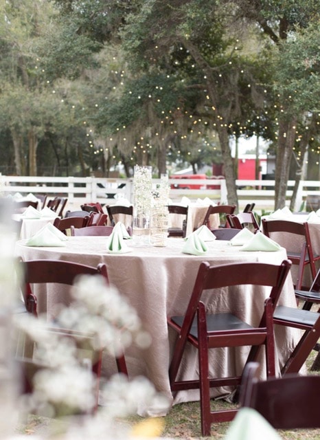 round tables with light brown linens set up outside of barn for wedding reception
